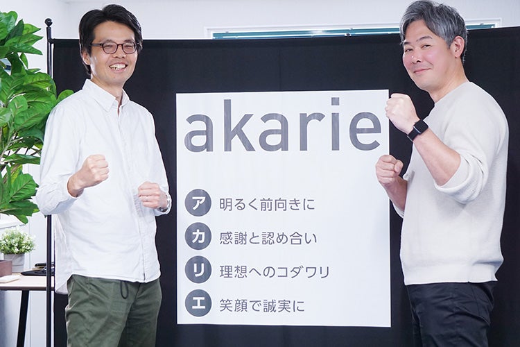 スローガンの前で挑戦ポーズをする田中さんと山根さん